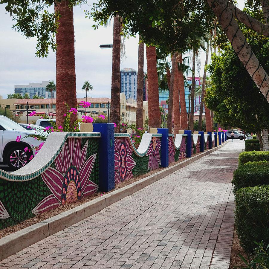 A palm tree-lined brick walkway bordered with low walls covered in mosaic tiles.