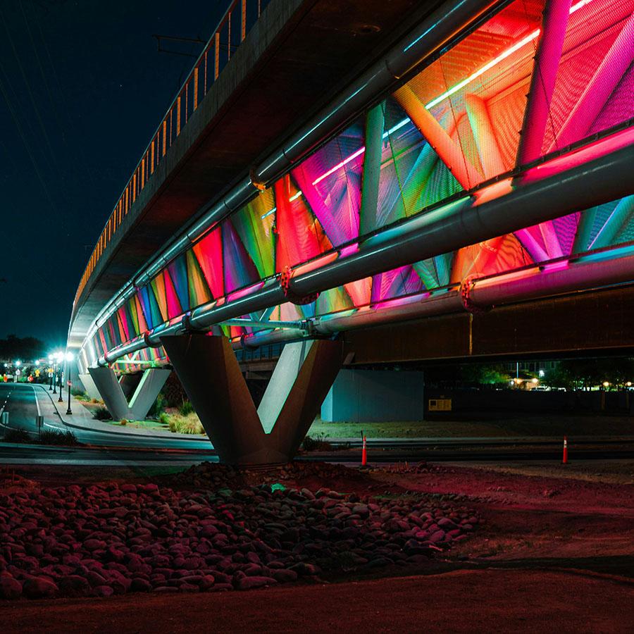The Tempe Town Lake pedestrian bridge colorfully lit at night.